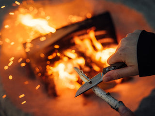 A man adding wood shavings to a beach bonfire with his Carted EDC slide lock folding pocket knife.