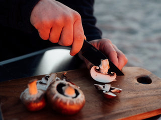 A man slicing mushrooms with his Hell Gap fixed blade camping knife on the beach.