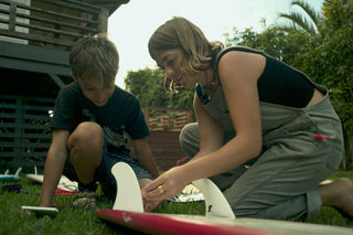 A woman helping a boy putting on surfboard fins.