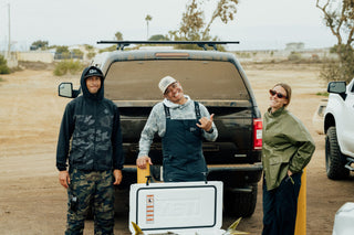 Three friends showing off their fish in a cooler behind their truck.