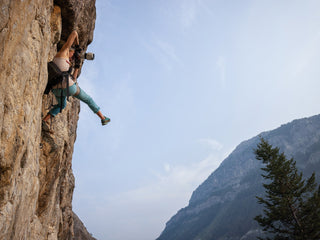 Professional rock climber and photographer Savannah Cummins up against a rock face taking a photo.