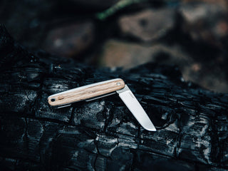 A Pike classic slip joint folding pocket knife resting on charcoal.