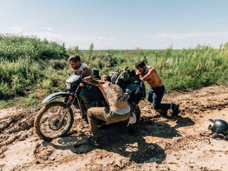 A group motorcyclist pushing a bike out of the mud.