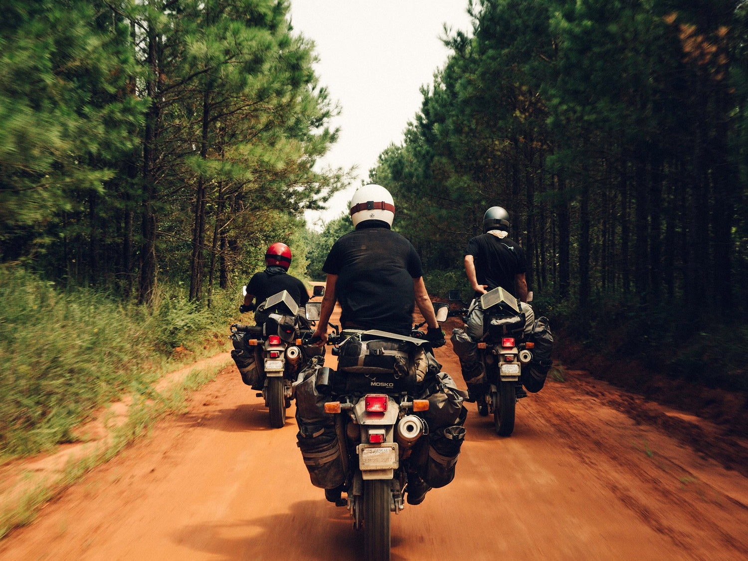 A group of motorcyclist headed down a red dirt road in the Arkansas wilderness.