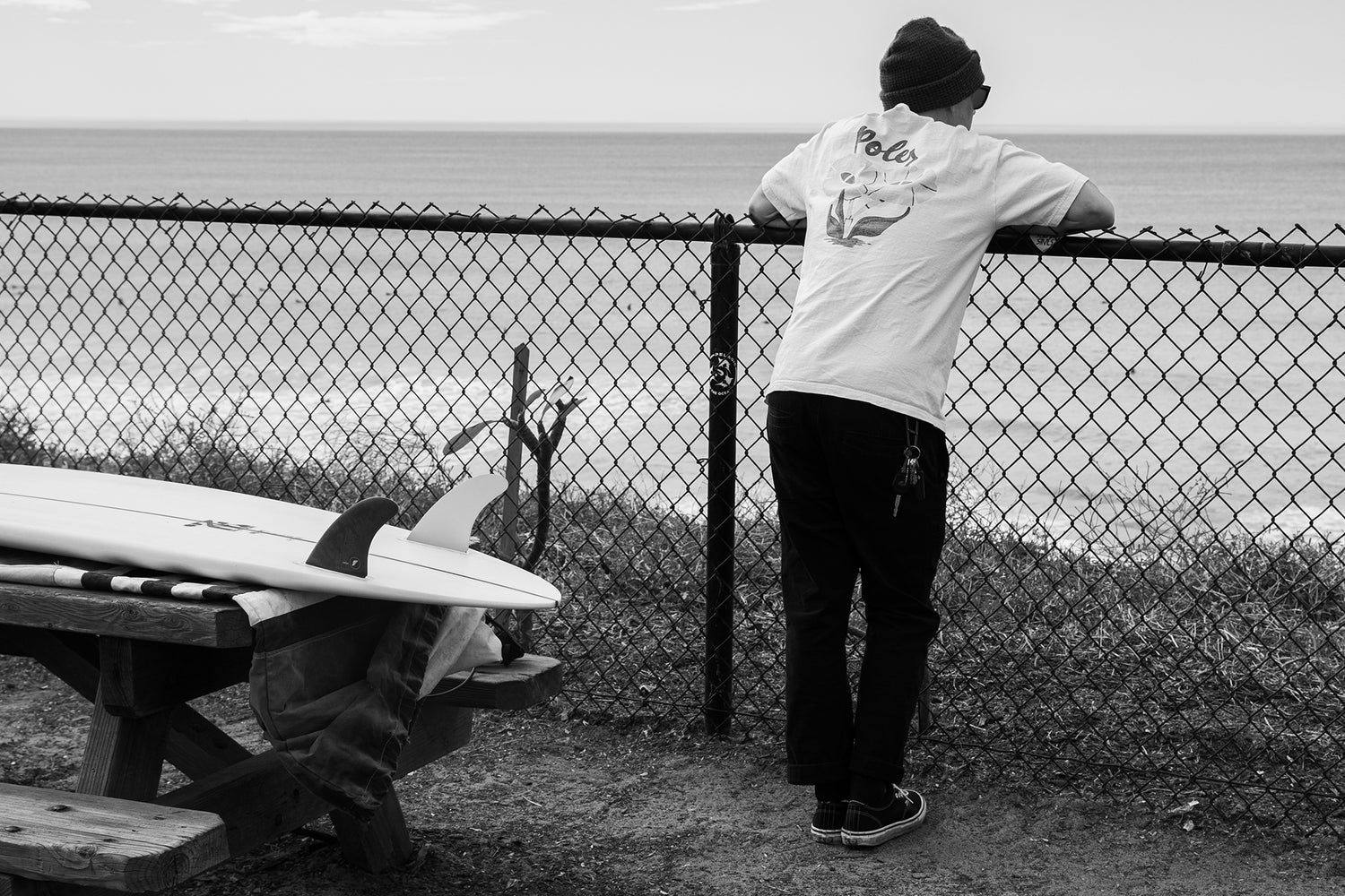 A man looking out to sea with his surfboard on a picnic table.