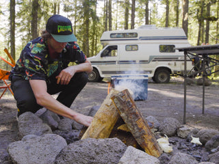 A man starting a camp fire with his RV in the background. 