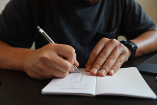 A man drawing with the Burwell EDC click pen in a notebook.