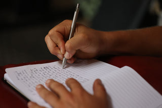 A person writing in a notebook with The Burwell EDC click pen.