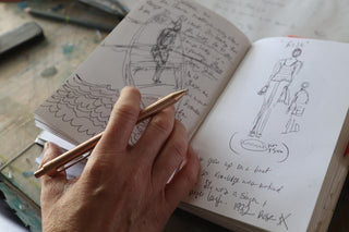 A woman sketching in a notebook with The Burwell EDC click pen.