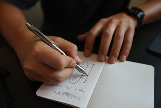 A man writing in a notebook with The Burwell EDC click pen.
