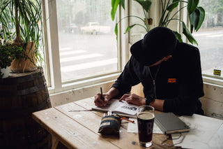 A man sketching in a notebook at a cafe with his Bolen titanium EDC twist pen.