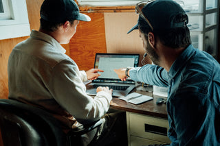 Two people designing a surfboard using a CAD program on a laptop in Nova Scotia, Canada.