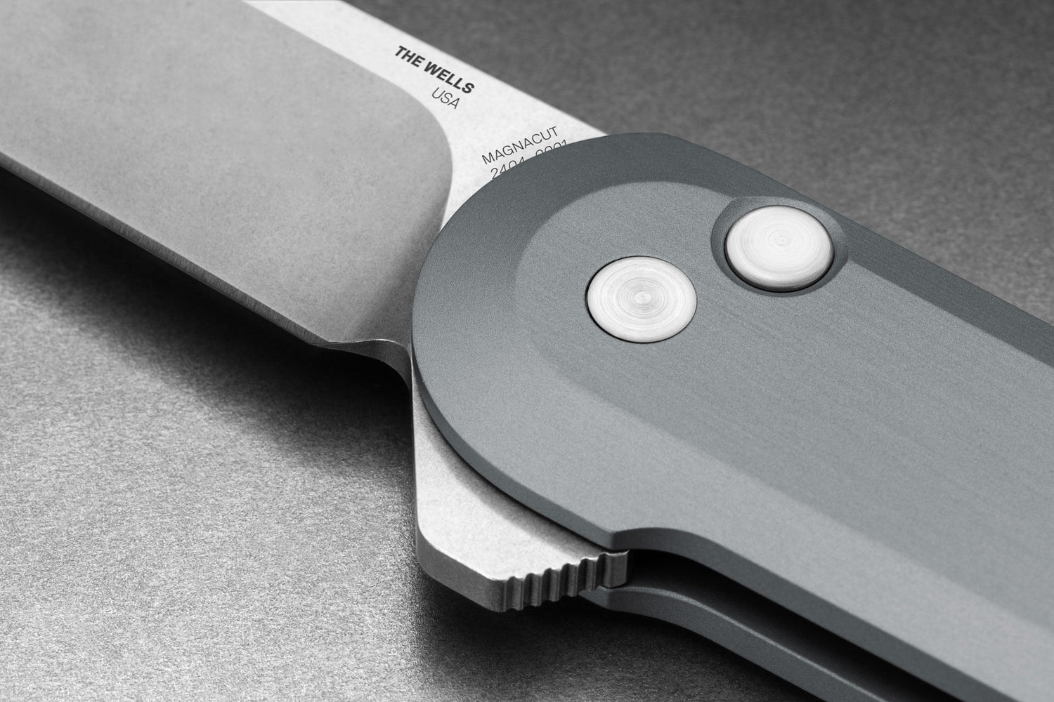 The pivot of the made in the USA Wells EDC button lock folding pocket knife in raw aluminum and Magnacut steel. 