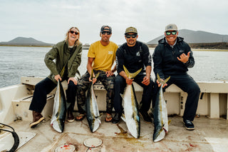 Four fishermen with their catch sitting on the side of the boat.