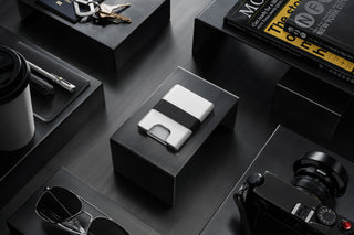 Silver wallet on a black box with keys and books in the background.