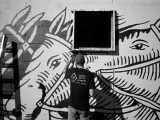 Artist Jess Mudgett painting a mural on an abandon building in the desert.