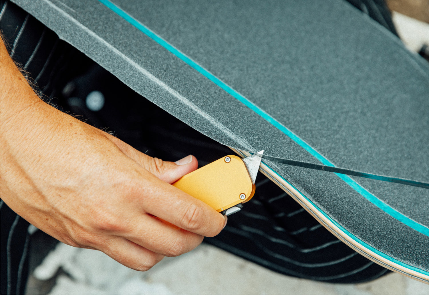 A man cutting the grip tape of his skateboard with a Palmer utility box cutter knife. 
