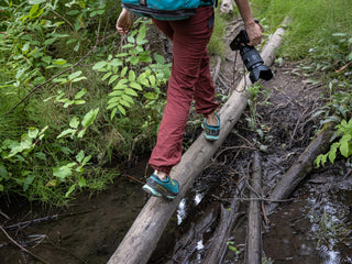 Professional rock climber and photographer Savannah Cummins walking on a log over a stream.