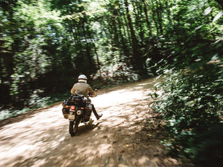 A motorcyclist riding on a dirt road through an Arkansas forest.