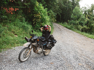 A motorcyclist taking a break on the side of a dirt road in the wilderness.