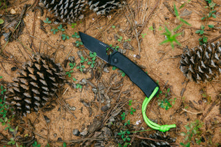 The Folsom EDC liner lock folding pocket knife in the dirt with pinecones. 